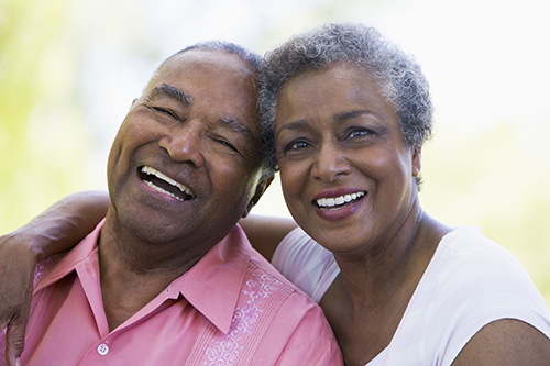 Elderly couple sitting outside with heads touching smiling and laughing